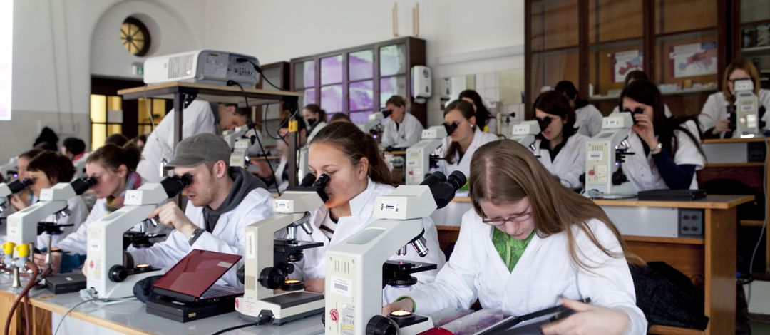 Foto: Studierende im Kittel beim Mikroskopieren im Hörsaal